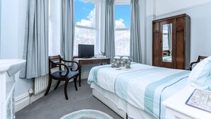 Una camera d'albergo con un letto, una scrivania con un computer, una sedia, un armadio e una finestra con tende.