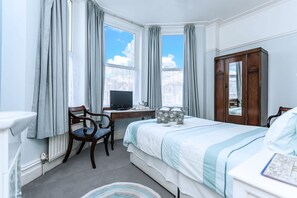 A hotel room with a bed, a desk with a computer, a chair, a wardrobe, and a window with curtains. - The Ravensbourne Hotel (Bournemouth)