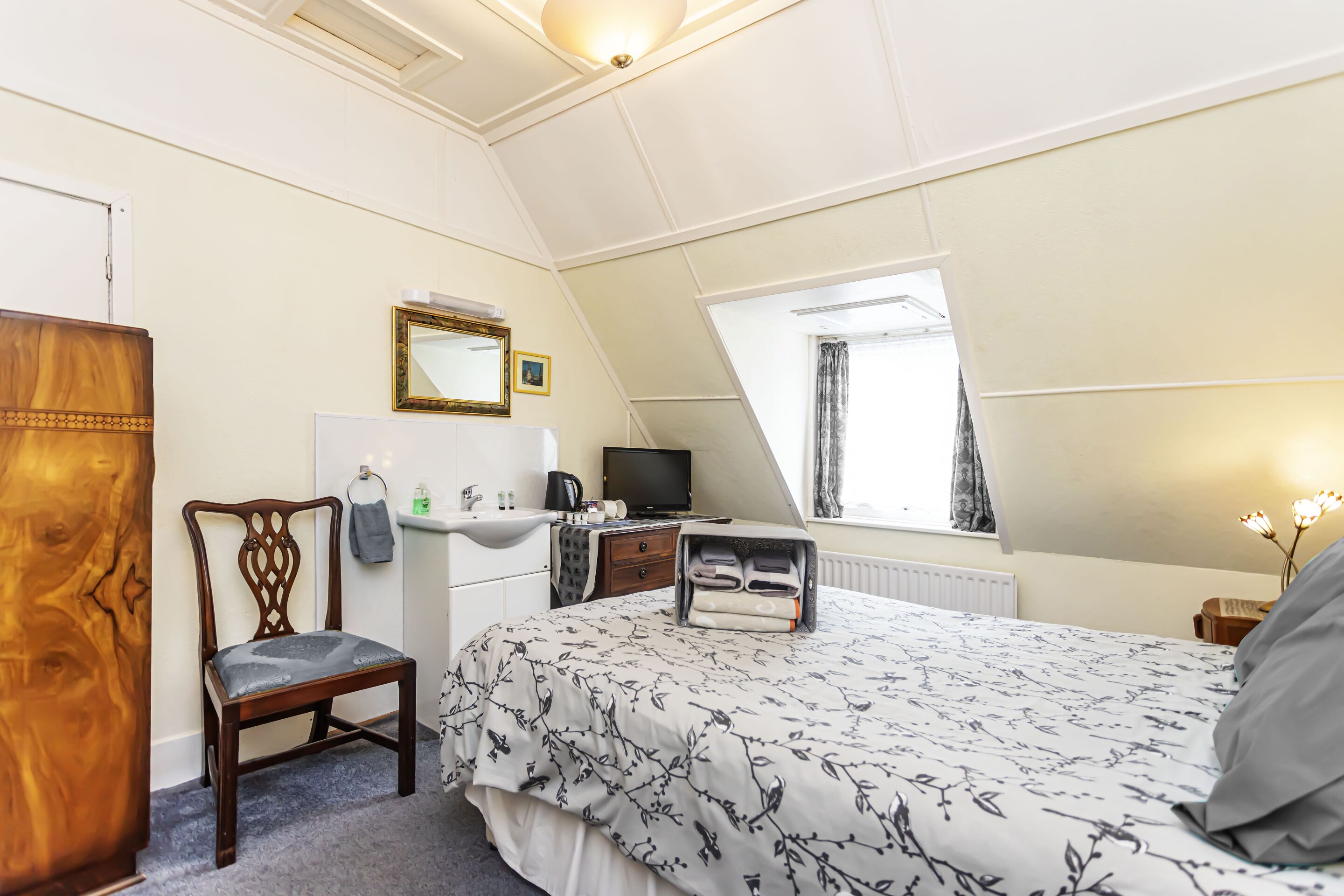 A bedroom with a bed, a chair, a desk, a television, a window, and a mirror.