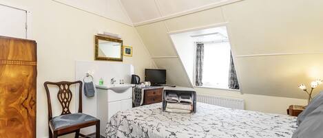 A bedroom with a bed, a chair, a desk, a television, a window, and a mirror.