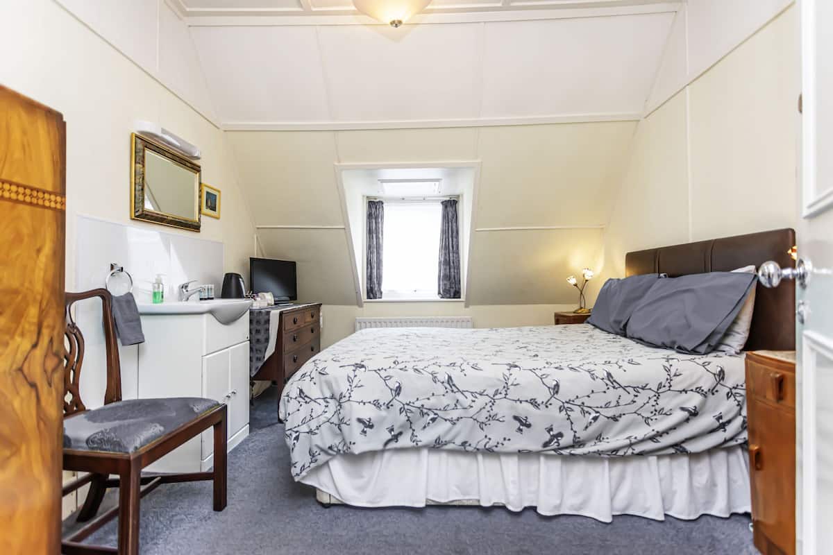 A bedroom with a bed, a desk, a chair, a television, and a window with curtains.