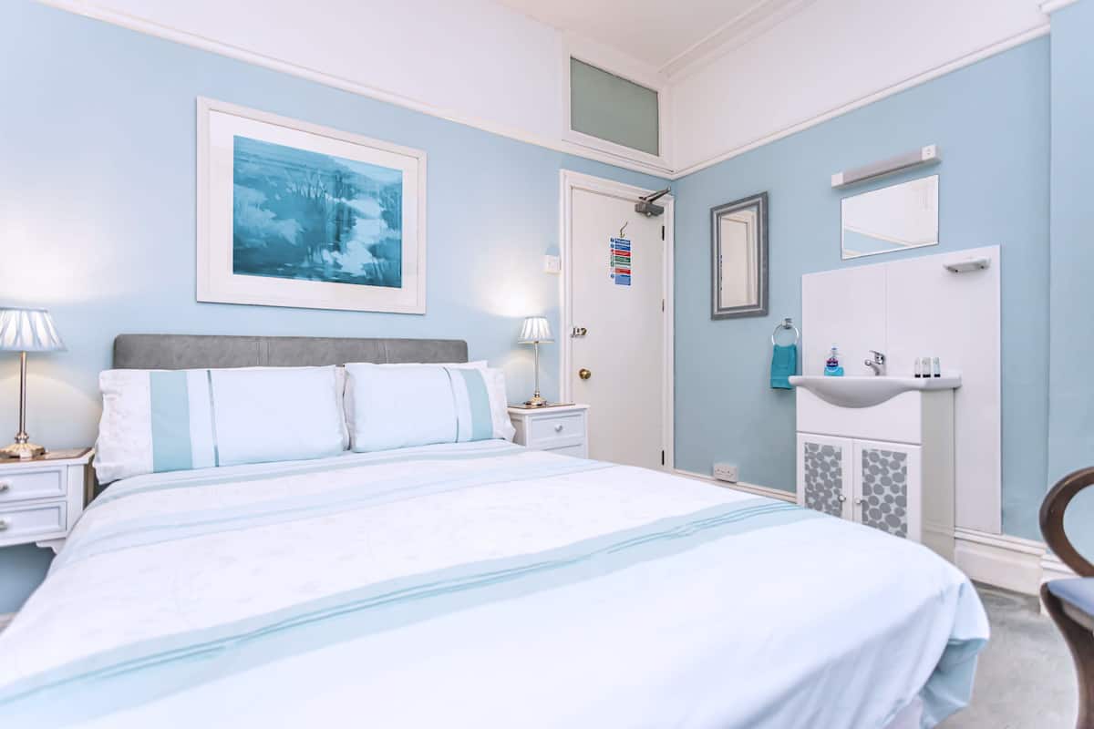 A neatly arranged bedroom with a bed, bedside tables, a nightstand, a dresser, a mirror, and a framed picture on the wall.