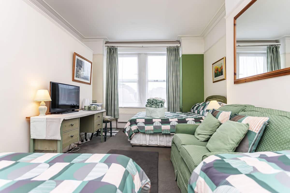 A hotel room with a bed, a desk with a television, a chair, and a window with curtains.