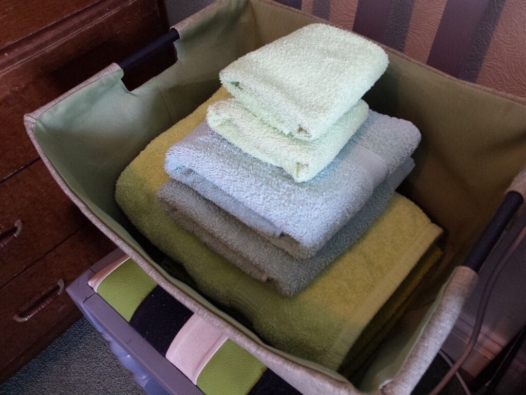 A storage bin with a handle, containing folded towels in various colors.
