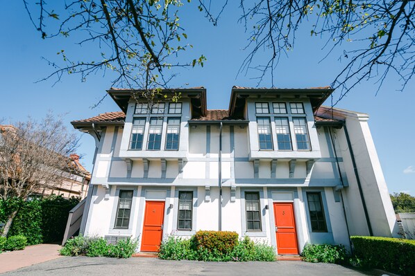 A two-story building with a symmetrical facade, featuring a central entrance flanked by two red doors, and a tiled roof. - Atterdag Inn (Solvang)