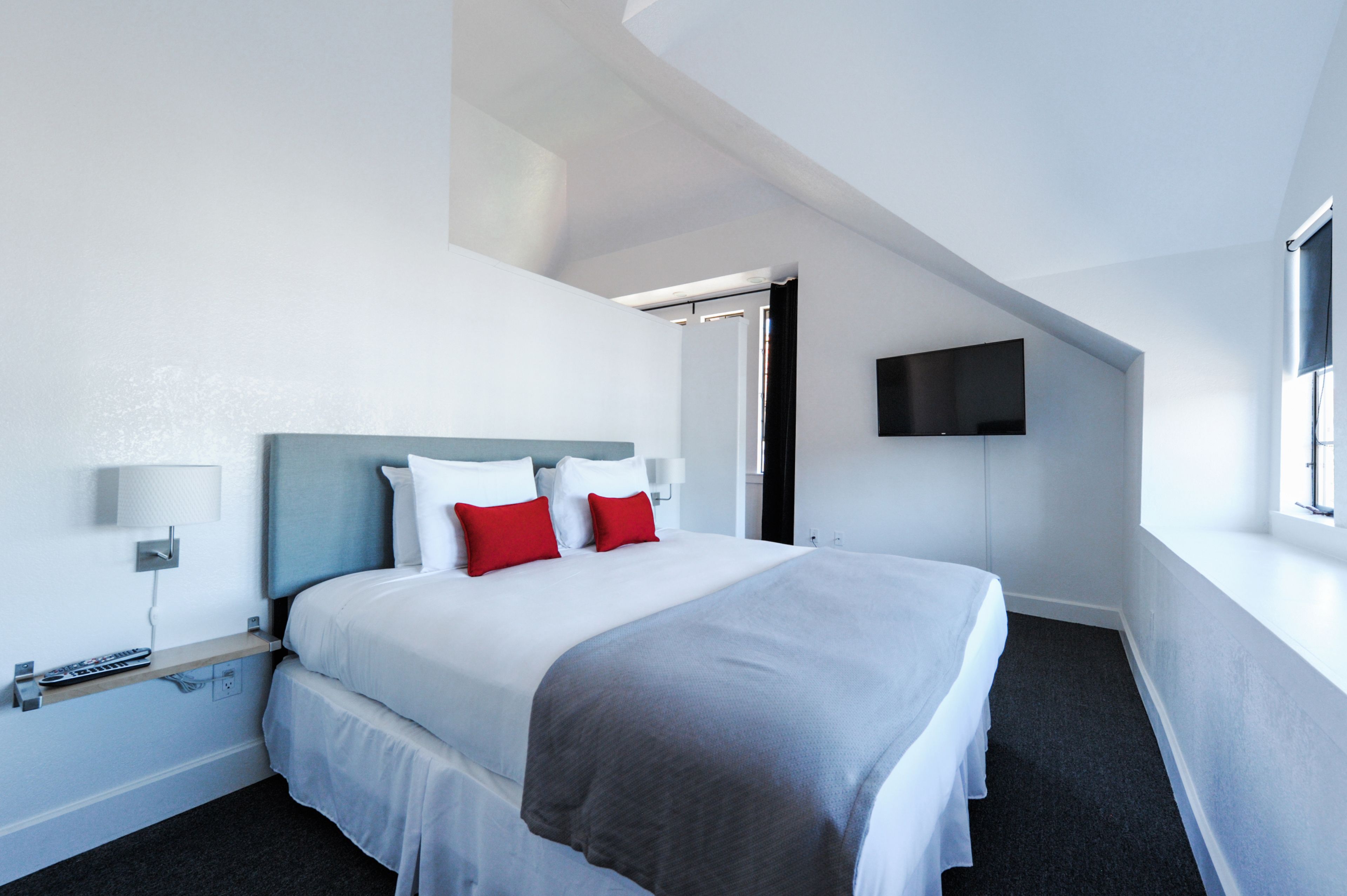 Una habitación de hotel moderna con una cama grande, un televisor montado en la pared y una ventana que proporciona luz natural.