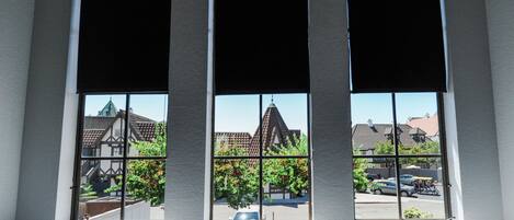 Drie ramen met zonwering, uitzicht op een woonwijk met huizen en een kerk.