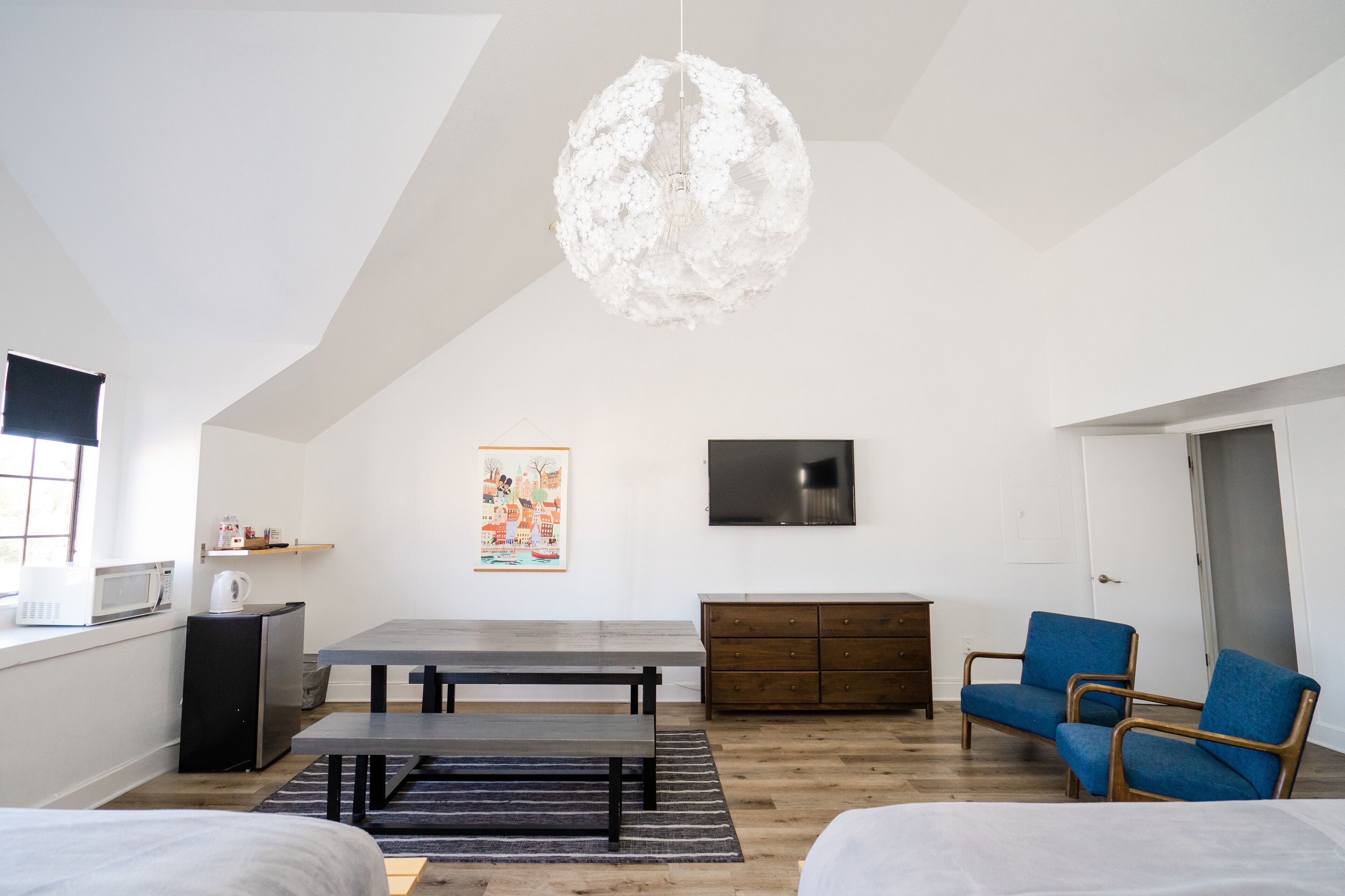 Una camera moderna e minimalista con un tavolo da pranzo, due sedie blu, un armadietto in legno, una televisione e un'originale lampada a sfera.