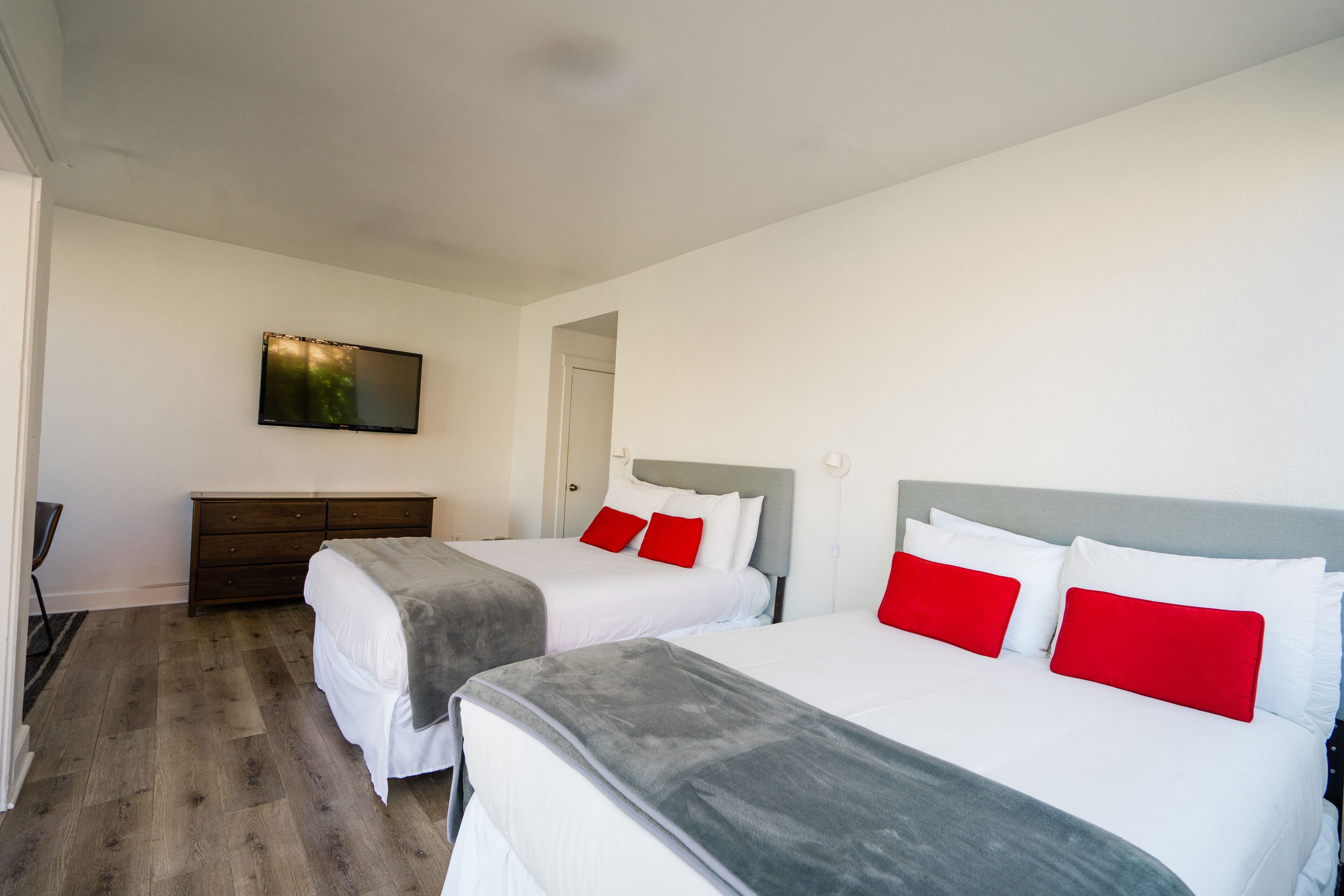 A hotel room with two beds, a flat-screen TV mounted on the wall, and a wooden floor.