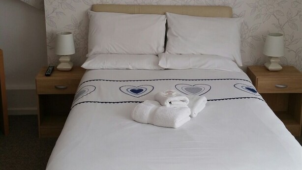 A neatly made bed with white linens, two pillows, and a folded towel. There are two bedside lamps on wooden nightstands. - Morrisy House (Blackpool)