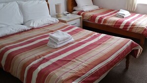 A hotel room with two beds, each with a striped bedspread and white pillows. There is a bedside table with a lamp and a phone. - Morrisy House (Blackpool)