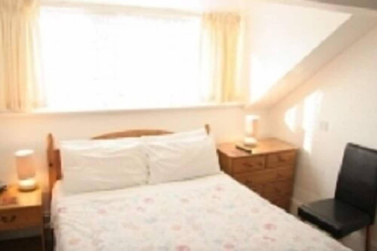A bedroom with a bed, a dresser, a chair, and a window with curtains.
