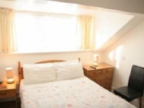 A bedroom with a bed, a dresser, a chair, and a window with curtains. - Morrisy House (Blackpool)