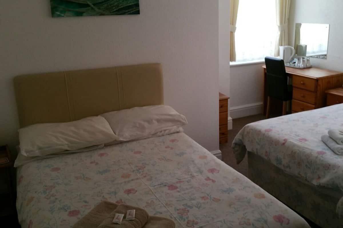 A hotel room with two beds, a desk, a chair, and a window with curtains.