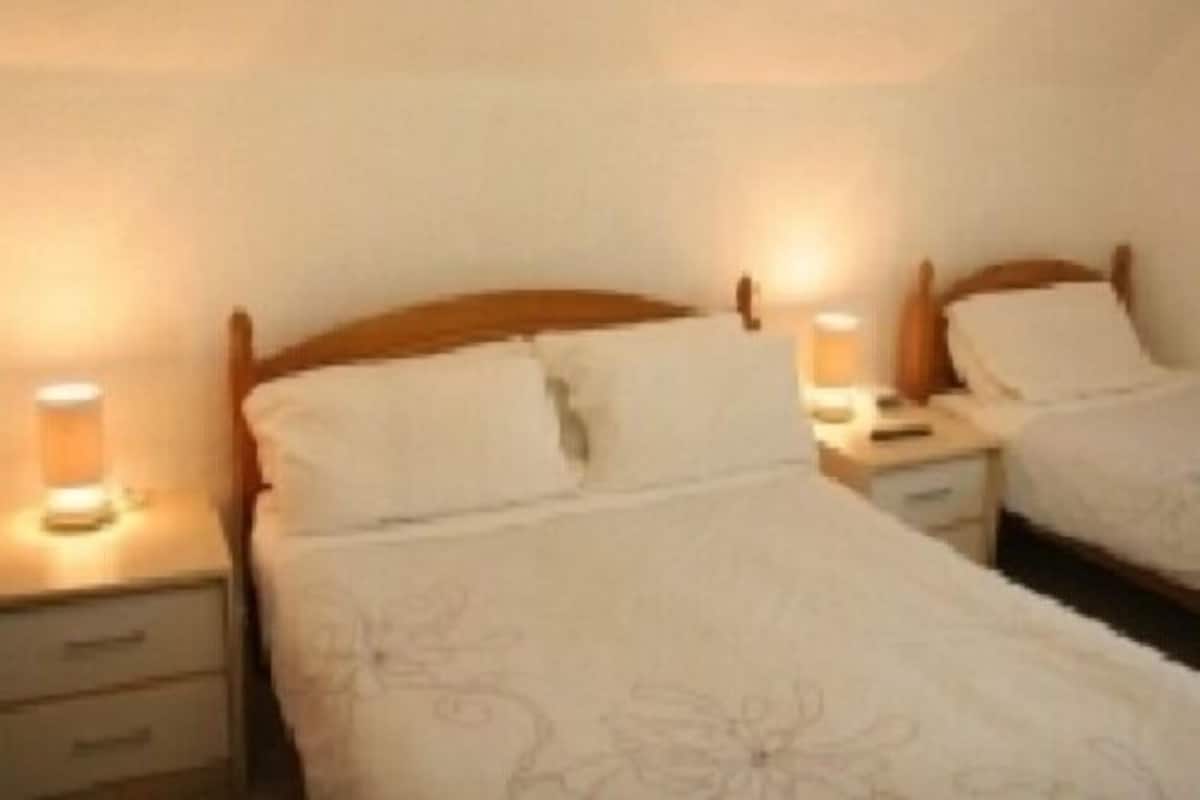 A hotel room with two single beds, each with a wooden headboard, a bedside table, and a lamp.