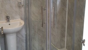 A bathroom with a glass-enclosed shower, a white pedestal sink, and marble walls. - Morrisy House (Blackpool)