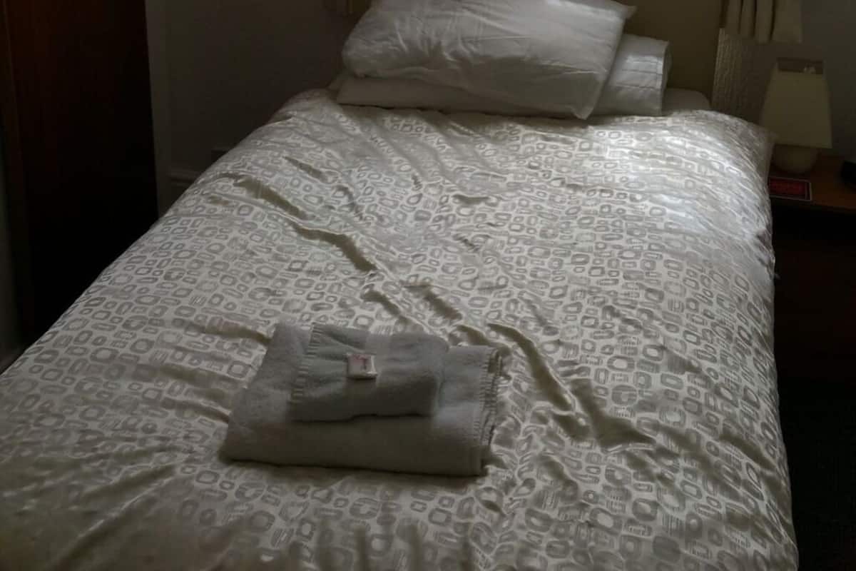 A single bed with a patterned bedspread and two pillows.