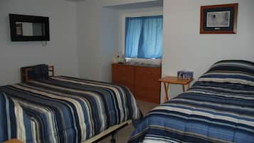 A bedroom with two beds, a dresser, a chair, a small table, a window with blue curtains, and a framed picture on the wall.