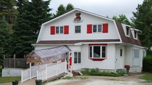 A two-story building with a red and white exterior, a covered front porch, and a small garden area. - Teddy Bear Bed & Breakfast (Bancroft)