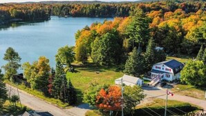 A house with a blue roof and white walls, surrounded by a forest and a lake. - Teddy Bear Bed & Breakfast (Bancroft)