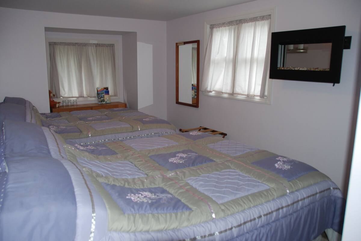 Un dormitorio con cama, una ventana con cortinas, un espejo y una mesita con objetos encima.
