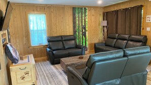 A cozy living room with a wooden interior, leather sofas, a small wooden cabinet, and a patterned rug. - Teddy Bear Bed & Breakfast (Bancroft)