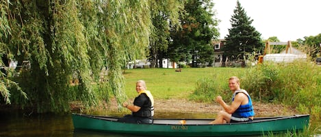 Dos personas en un canoa verde sobre un río tranquilo, rodeado de exuberante vegetación y árboles.