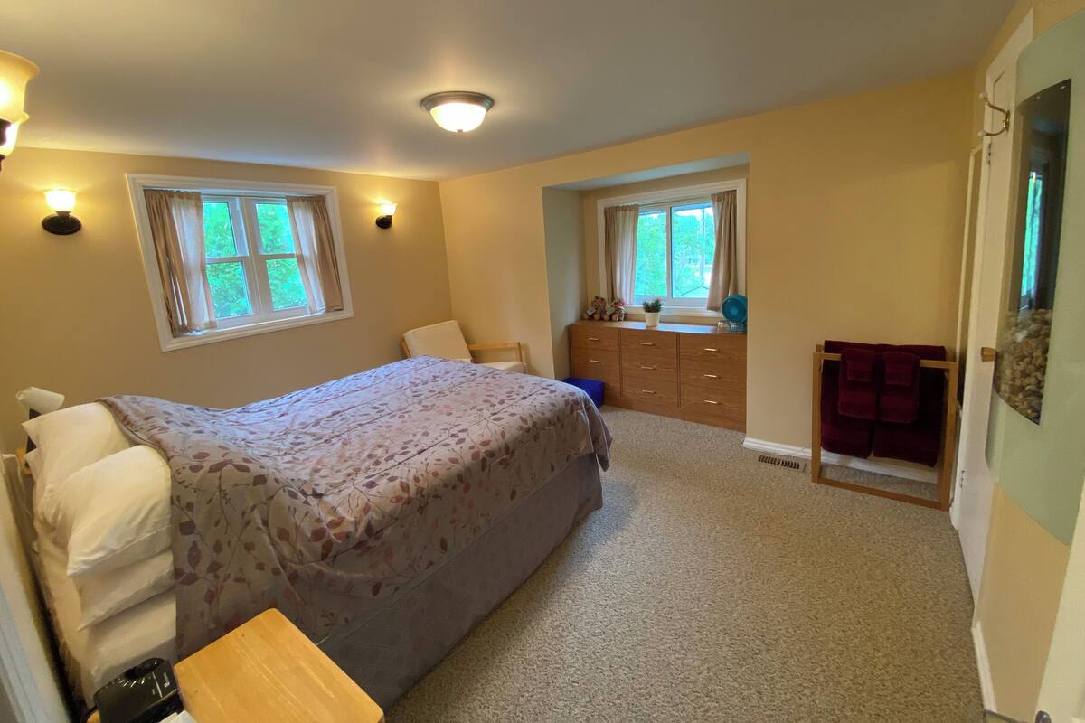 Un dormitorio con cama, cómoda y dos ventanas.