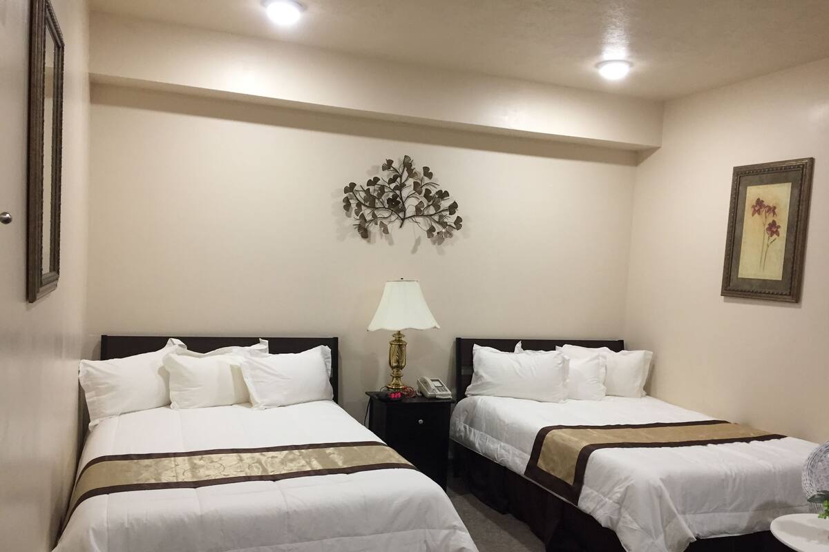 Une chambre d’hôtel avec deux lits, une table de chevet avec une lampe, une horloge murale et un tableau encadré.