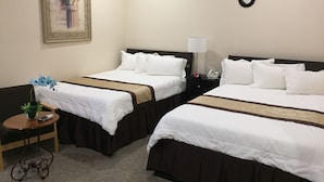 A hotel room with two beds, a nightstand with a lamp, a small table with a plant, and a framed picture on the wall.