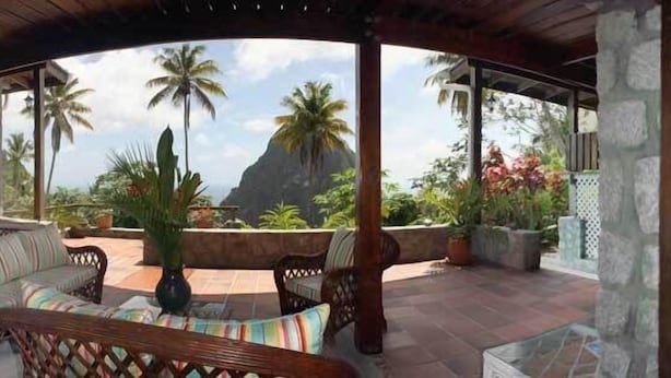 A covered outdoor seating area with a view of palm trees and a mountain.