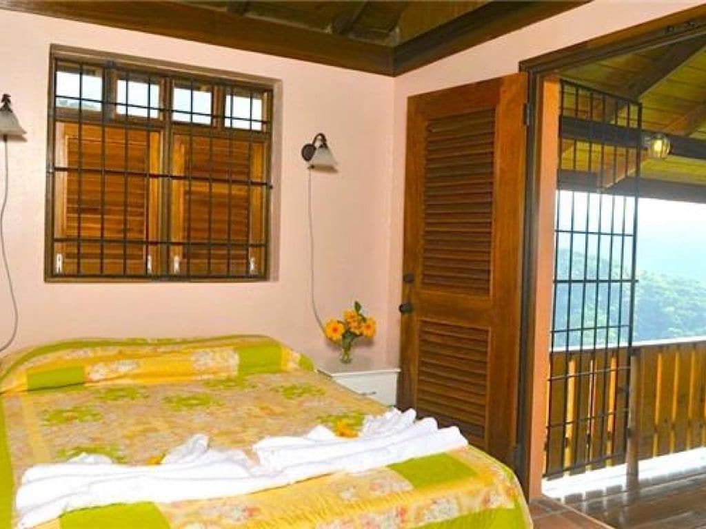 A bedroom with a bed, a window with bars, a door, and a view of the outdoors.