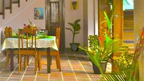 A dining area with a table set for four, surrounded by chairs. There is a staircase with wooden railings leading to an upper level. A potted plant is visible in the foreground. - Piton Deck Villa (Soufrière)