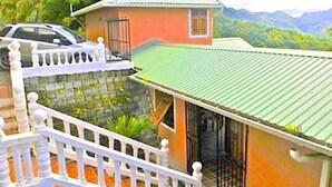 A two-story building with a green roof, a balcony with white balustrades, and a car parked in front. - Piton Deck Villa (Soufrière)