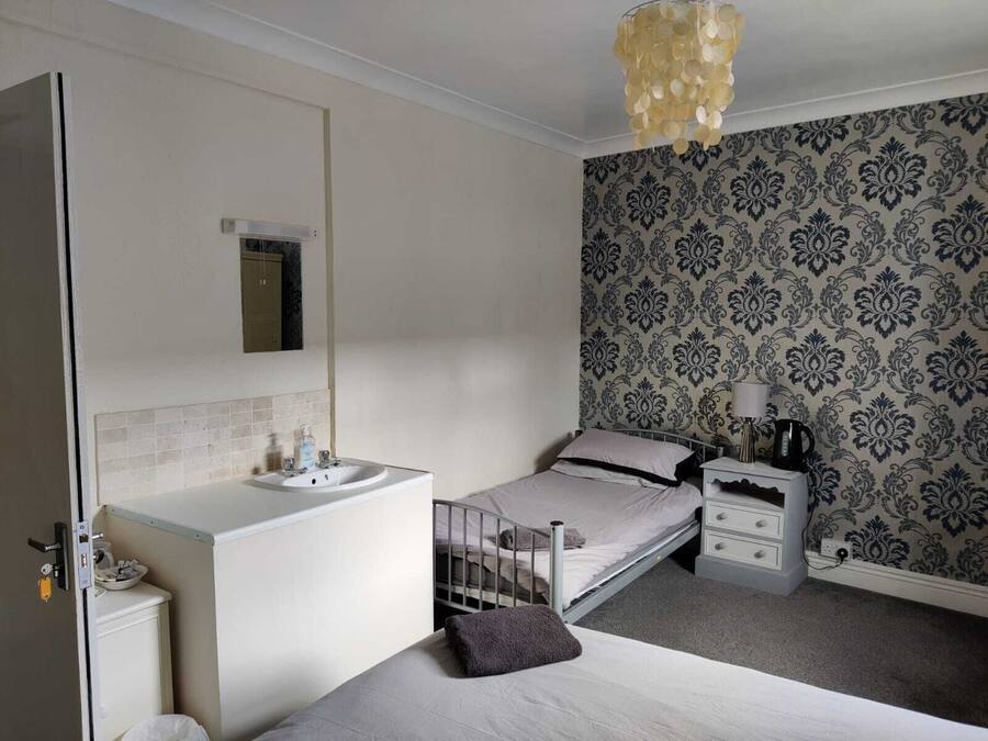 Un dormitorio con una cama individual, una mesita de noche, un tocador y un baño con lavamanos e inodoro.