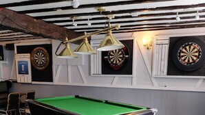 Una mesa de billar con superficie de fieltro verde, una mesa de pool y tres dardos colgados en la pared.