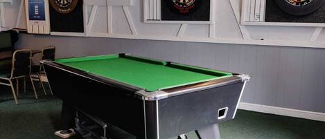 A billiards table with a green felt surface, a pool table, and three dartboards mounted on the wall.