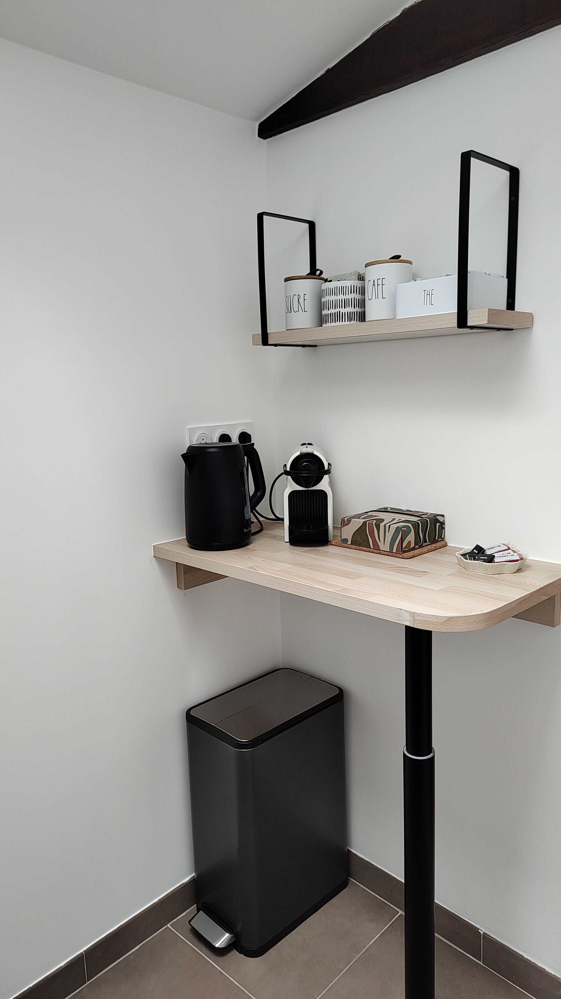 Una kitchenette compacta con cafetera, hervidor y recipientes de almacenamiento sobre una encimera de madera.