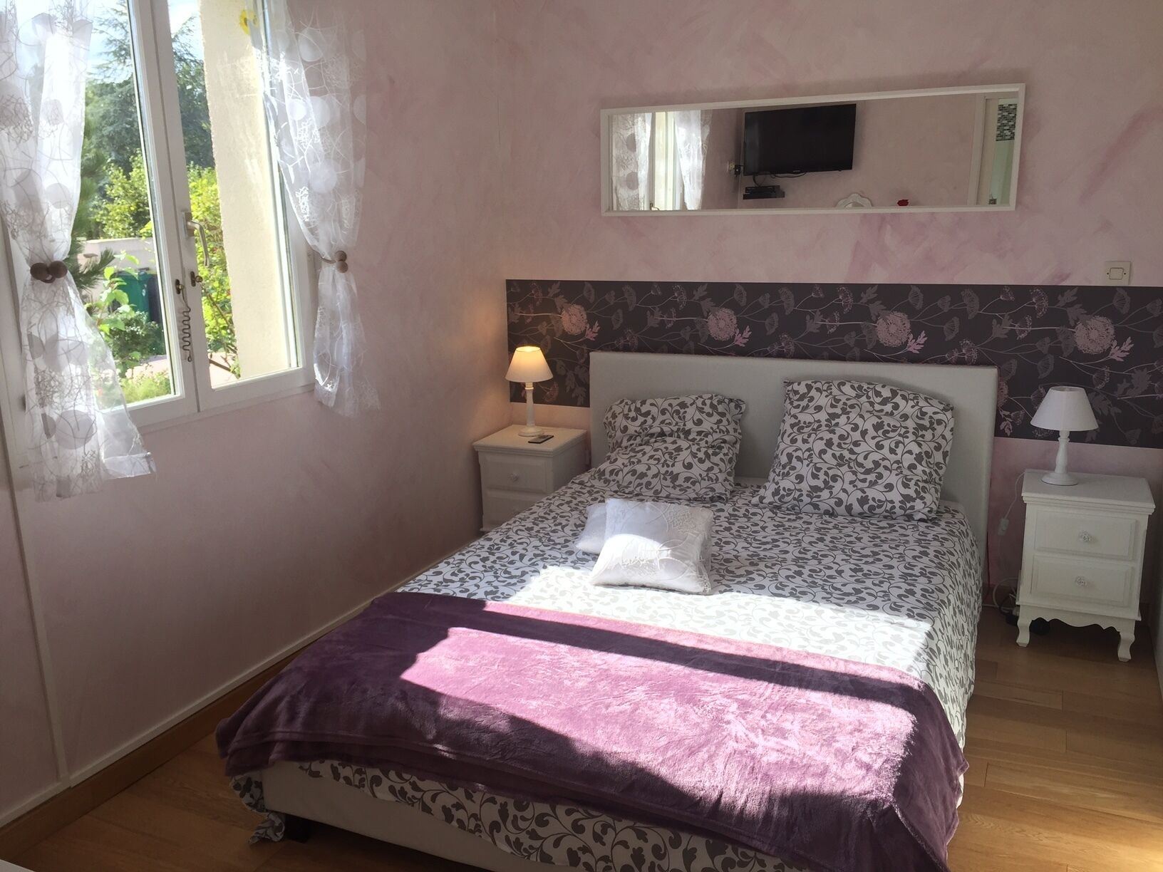 Quarto com cama, duas mesas de cabeceira, televisão e janela com cortinas.