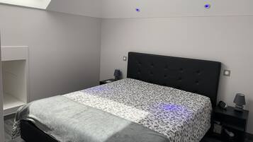 A bedroom with a bed, a nightstand, a lamp, and a skylight.