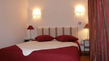 Una cama bien hecha con una colcha roja y blanca, dos lámparas de noche y una mesita de noche con lámpara.