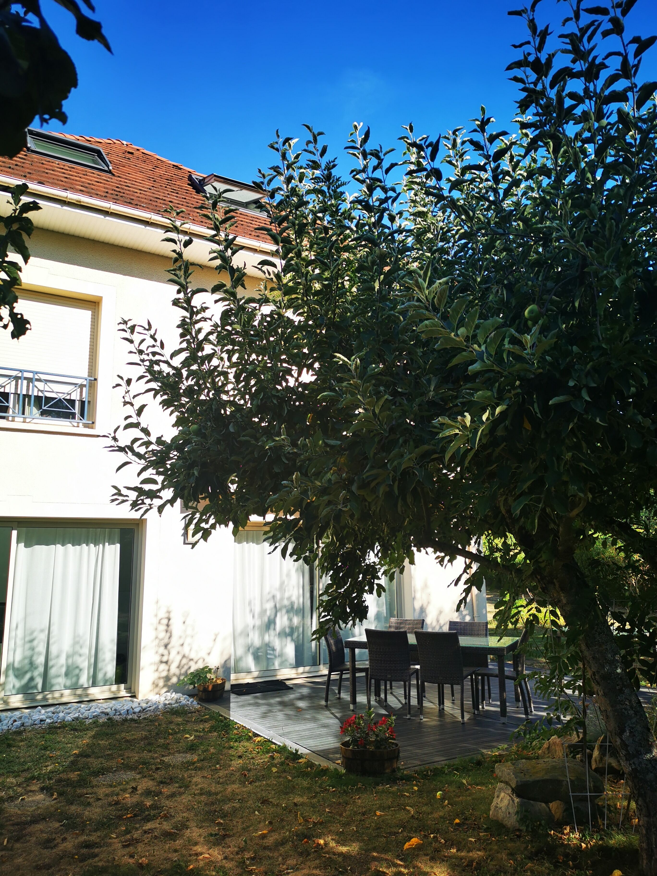 A patio with a table and chairs, a small garden, and a building with a tiled roof.