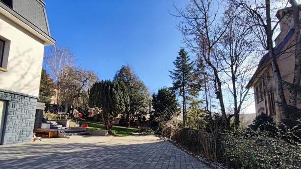 Une cour dallée avec un chemin en briques, entourée d’arbres et de bâtiments.