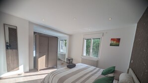 Une chambre à coucher comprenant un grand lit, une armoire, un radiateur, une fenêtre et une porte donnant sur un espace extérieur.