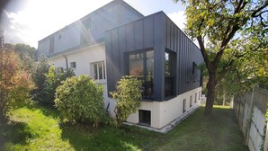Une maison moderne à deux étages, dotée d’un toit plat, de grandes fenêtres et d’un jardin bien entretenu.