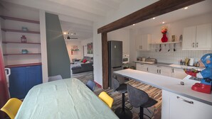 Une cuisine moderne avec des armoires blanches, un four encastré et un réfrigérateur. On y trouve un coin repas avec une table et des chaises, ainsi qu’un salon avec un canapé et une table basse.