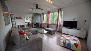 Un salon moderne avec un canapé, un pouf et un téléviseur posé sur un meuble blanc.