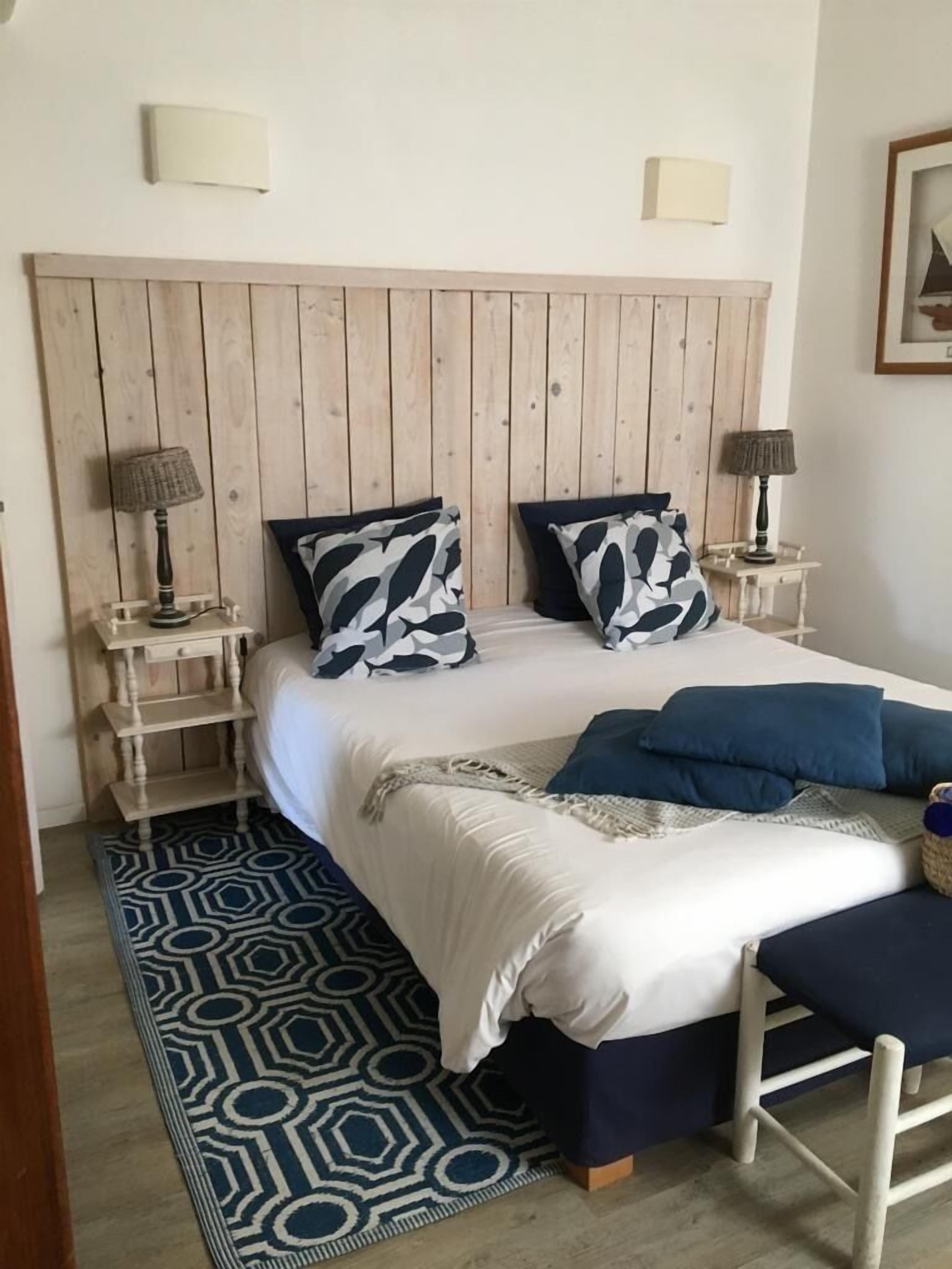 Une chambre à coucher avec une tête de lit en bois, deux tables de chevet avec des lampes, un tapis à motifs et un banc.