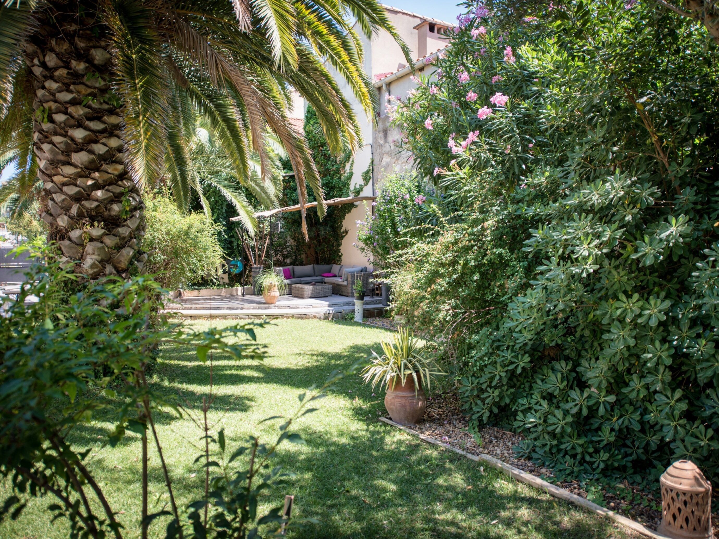 A well-maintained garden with a stone pillar, a seating area with cushions, and various plants.