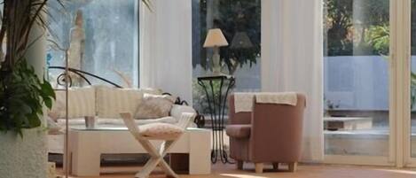 A sunlit room with a pool, a sofa, a chair, and a lamp.